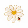 Daisy brooch with gold-tone metal outline, white enamel petals, yellow stone center, and red ladybird charm. Cutout on white background.