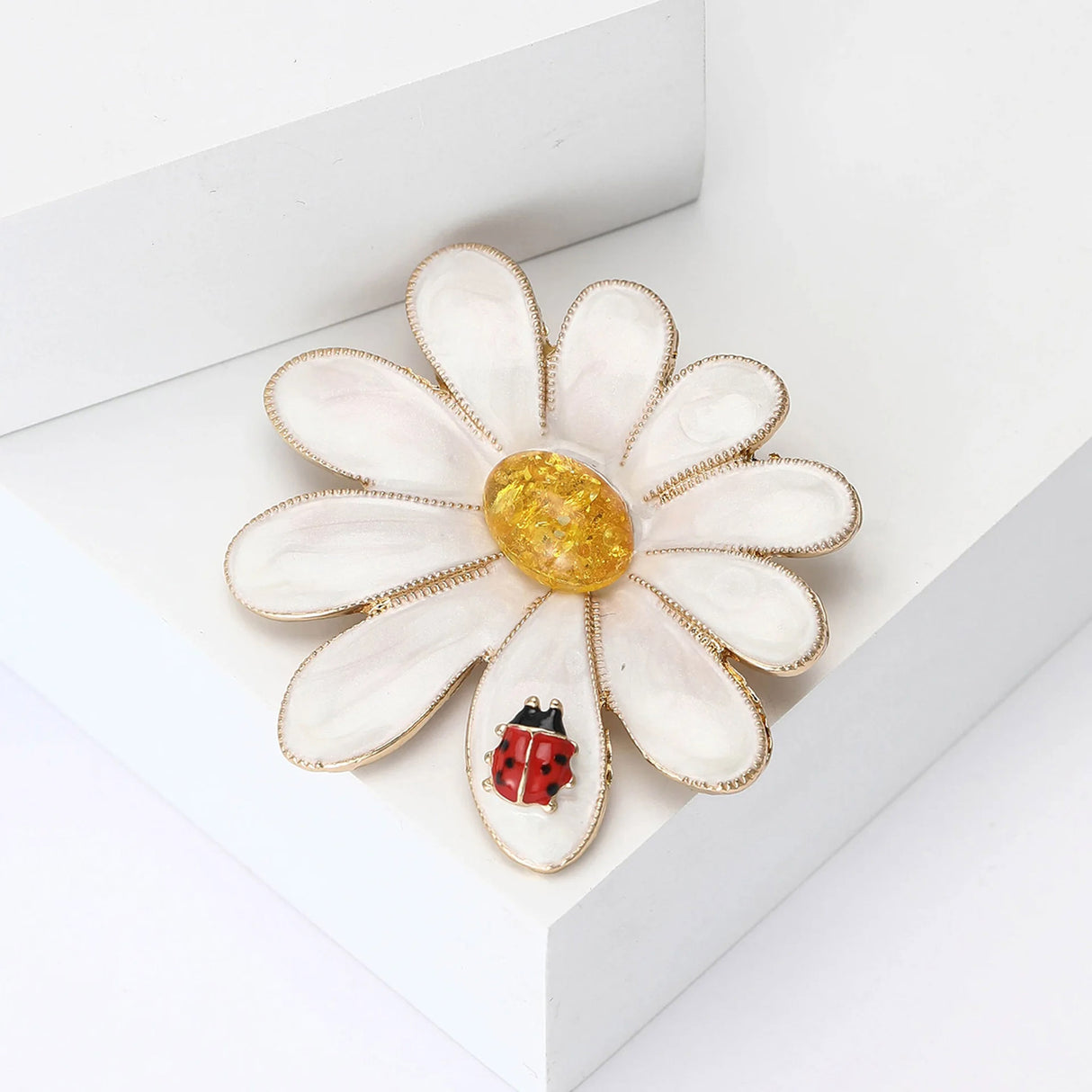Daisy brooch with gold-tone edges, white enamel petals, yellow center stone, and red ladybug accent, angled view.