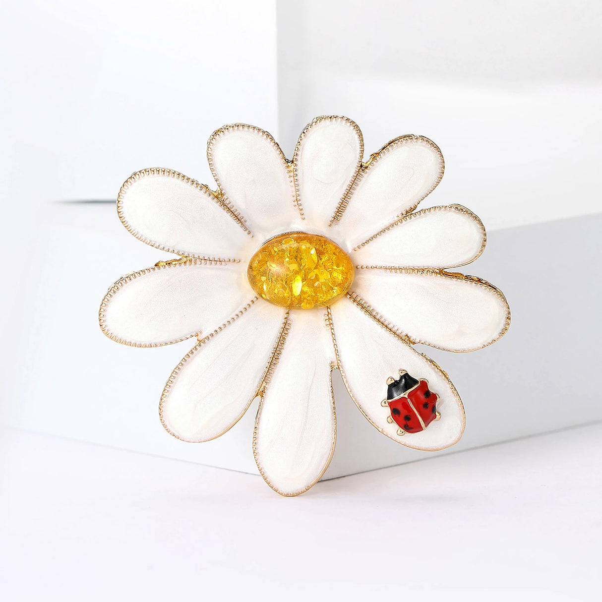 Daisy brooch featuring gold-tone trim, white petals, a textured yellow center, and red ladybird detail, upright pose on white.