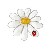 Daisy brooch with silver-tone edges, white glossy petals, yellow textured center stone, and red ladybird figure, cutout on white.