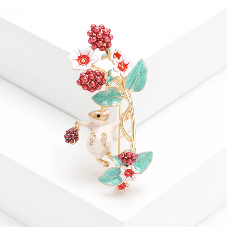 Mouse brooch with pearl-toned body, red bead berry clusters, white and red flowers, and green leaves, upright view on white steps in studio.