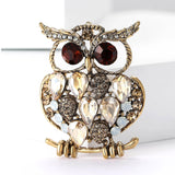 Owl brooch with gold-tone finish, beige teardrop stones, red eyes, and round white accents, front view on white background.