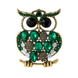 Owl brooch with gold-tone finish, large green faceted stones, black round eyes, and small multicolor rhinestone accents. Cutout on white.