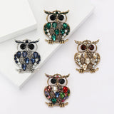 Set of four owl brooches in silver and gold-tone finishes with blue, green, beige, and multicolor stones. Flat lay on white background.