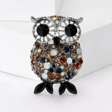 Owl brooch with silver-tone metal, large black eyes, and round pave stones in shades of brown, blue, and white, finished with black pointed oval feet, upright view on white background.