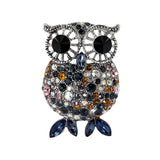 Owl brooch with silver-tone detailing, large black eyes, and blue, orange, pink, and iridescent faceted stones. Blue marquise-cut stones for feet. Cutout on white.