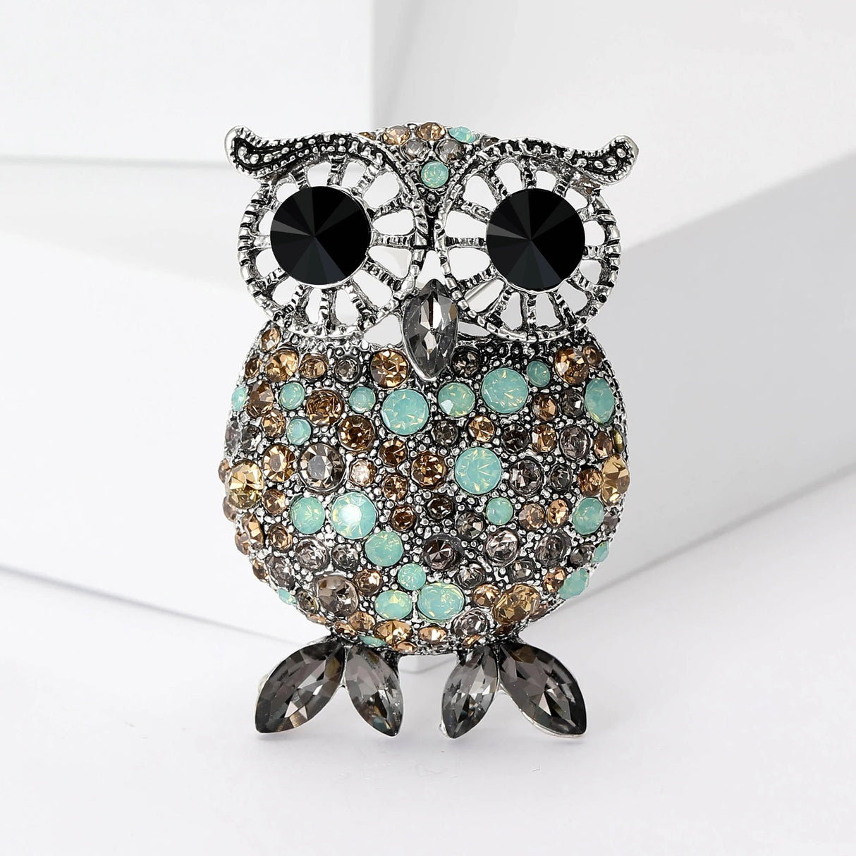 Owl brooch with silver-tone finish, black eyes, and round faceted stones in turquoise, beige, and gray, completed with gray marquise-cut feet, upright pose on white background.