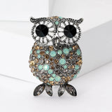 Owl brooch with silver-tone finish, black eyes, and round faceted stones in turquoise, beige, and gray, completed with gray marquise-cut feet, upright pose on white background.