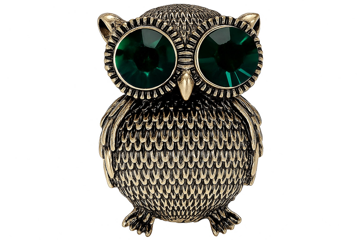 Owl brooch with textured gold-tone metal finish and large green faceted stone eyes, cutout on white background. Landscape crop for secondary use.