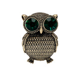 Owl brooch with textured gold-tone metal finish and large green faceted stone eyes, cutout on white background.