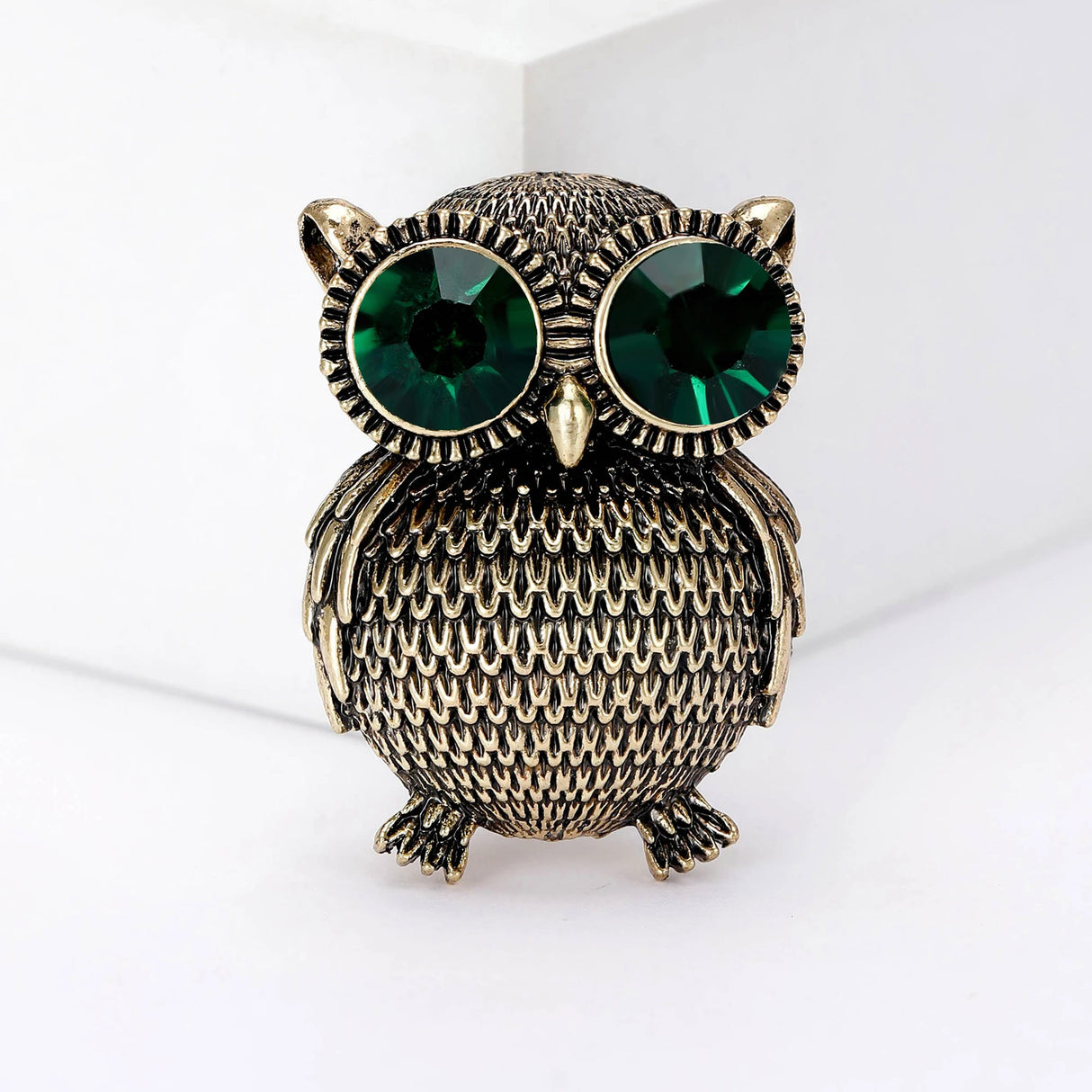 Owl brooch in gold-tone finish with textured body and oversized green faceted eyes, upright front view.