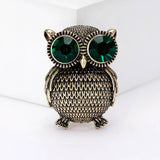Owl brooch in gold-tone finish with textured body and oversized green faceted eyes, upright front view.