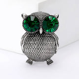 Owl brooch with silver-tone textured metal finish and prominent green faceted stone eyes, front studio view.