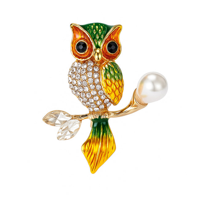 Owl brooch with green and gold-tone finish, clear faceted stones, and pearl-like bead on branch, cutout on white.