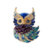 Owl brooch with gold-tone outline, blue and green enamel feathers, clear faceted stones, and round blue eyes, cutout on white.