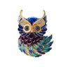 Owl brooch with gold-tone outline, blue and green enamel feathers, clear faceted stones, and round blue eyes, cutout on white.