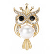 Owl brooch with gold-tone metal finish, black crystal eyes, clear round faceted stone accents, and large white round faux pearl body, cutout on white.