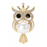 Owl brooch with gold-tone metal finish, black crystal eyes, clear round faceted stone accents, and large white round faux pearl body, cutout on white.