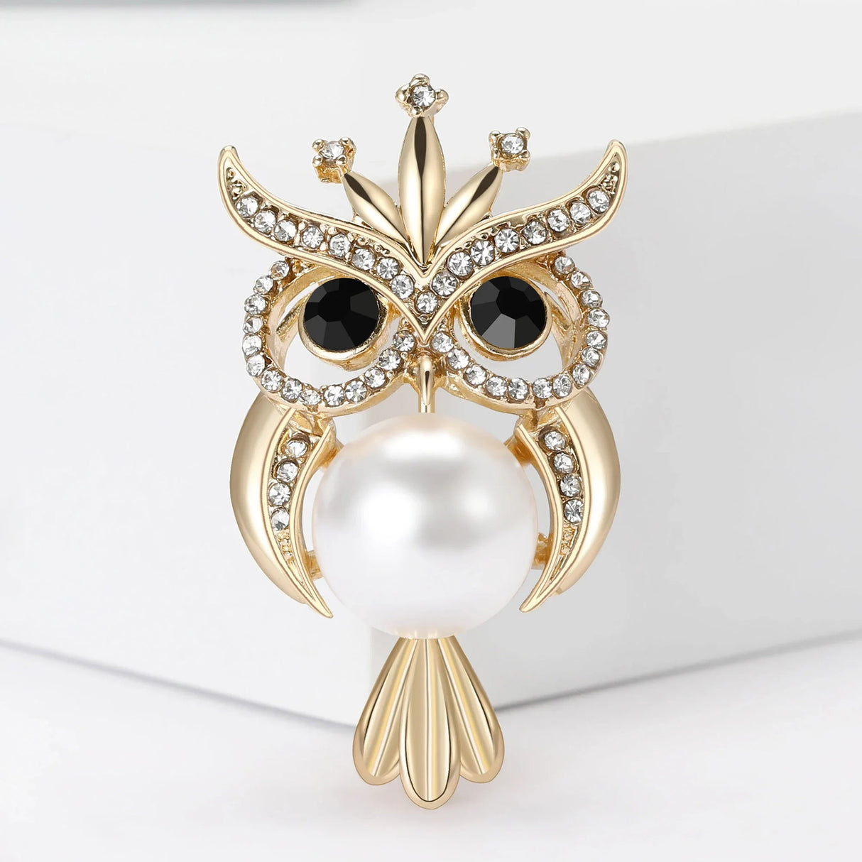 Owl brooch with gold-tone finish, round eyes made from black crystals, small clear faceted stone accents, and large white bead body, front view.