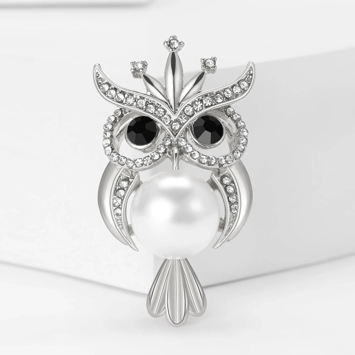 Owl brooch in silver-tone metal with clear rhinestone accents, black eyes, and large white faux pearl body, front view on white background.
