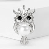 Owl brooch in silver-tone metal with clear rhinestone accents, black eyes, and large white faux pearl body, front view on white background.