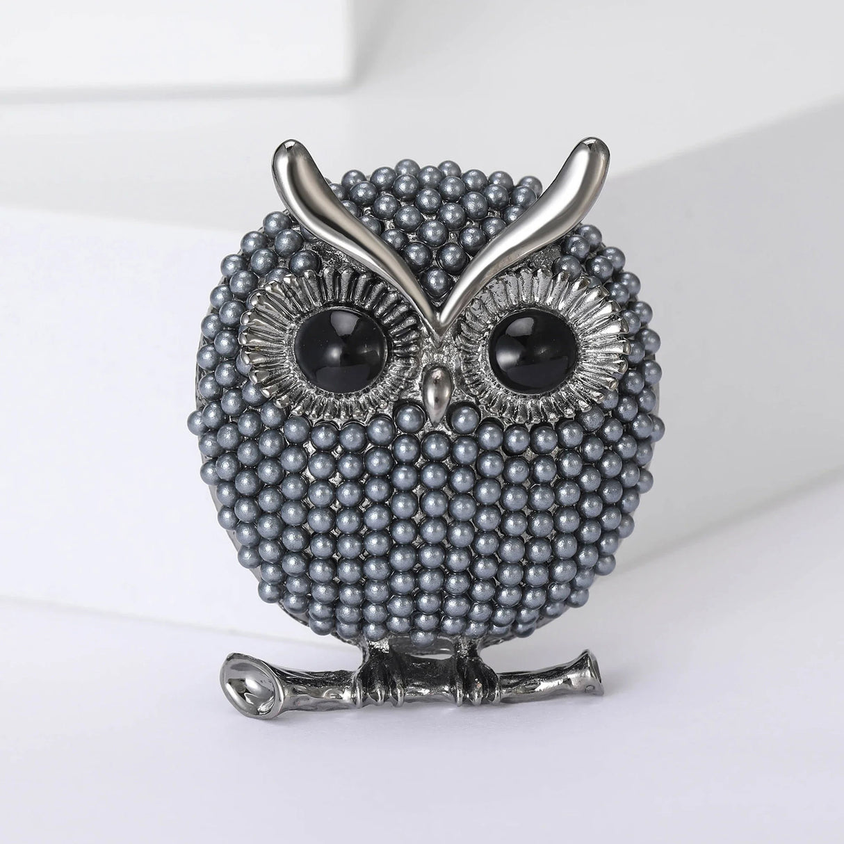 Owl brooch with small gray round beads, black eyes, and silver-tone accents, upright pose on white surface.