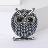 Owl brooch with small gray round beads, black eyes, and silver-tone accents, upright pose on white surface.