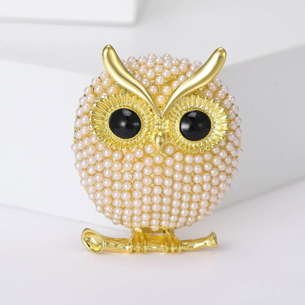 Owl brooch with body covered in small round beads, black eyes, and gold-tone finish, upright view on white background.