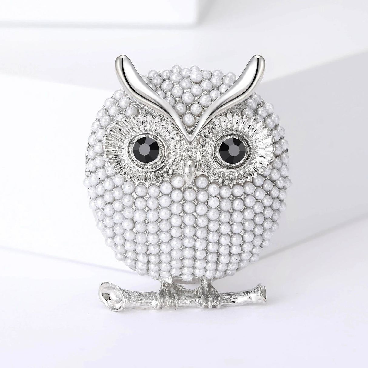Owl brooch with white round beads, black eyes, and silver-tone metal details, upright pose on white platform.