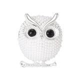 Owl brooch with silver-tone finish, white round beads, black gem-like eyes, and perch design, cutout on white background.