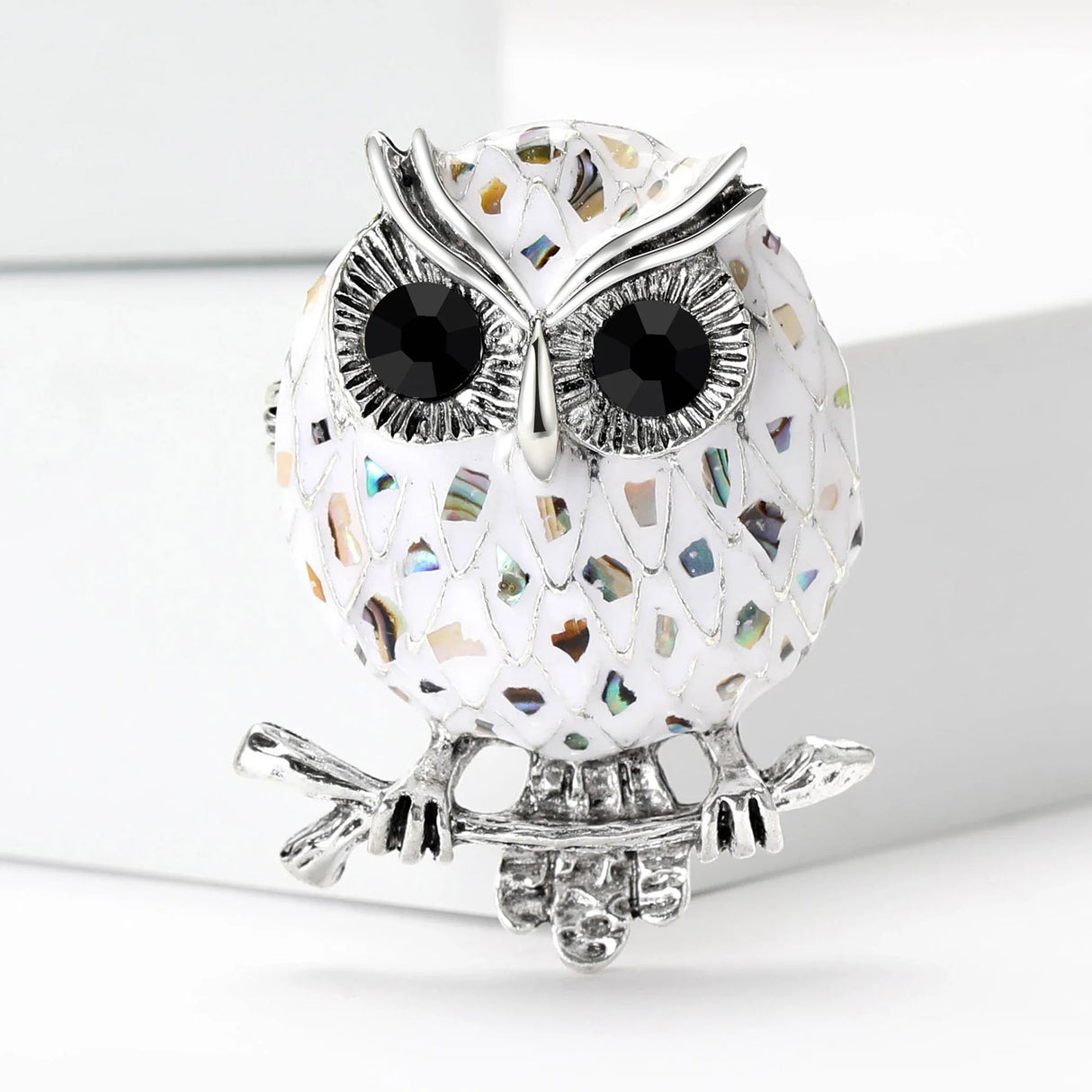 Owl brooch with white-tone mosaic body resembling abalone shell, multicolor reflective accents, and silver-tone branch perch, cutout on white.