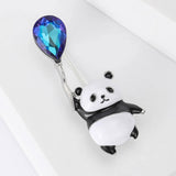 Panda brooch with black and white enamel, holding a blue and purple faceted balloon-shaped stone, angled bird's eye view on white.