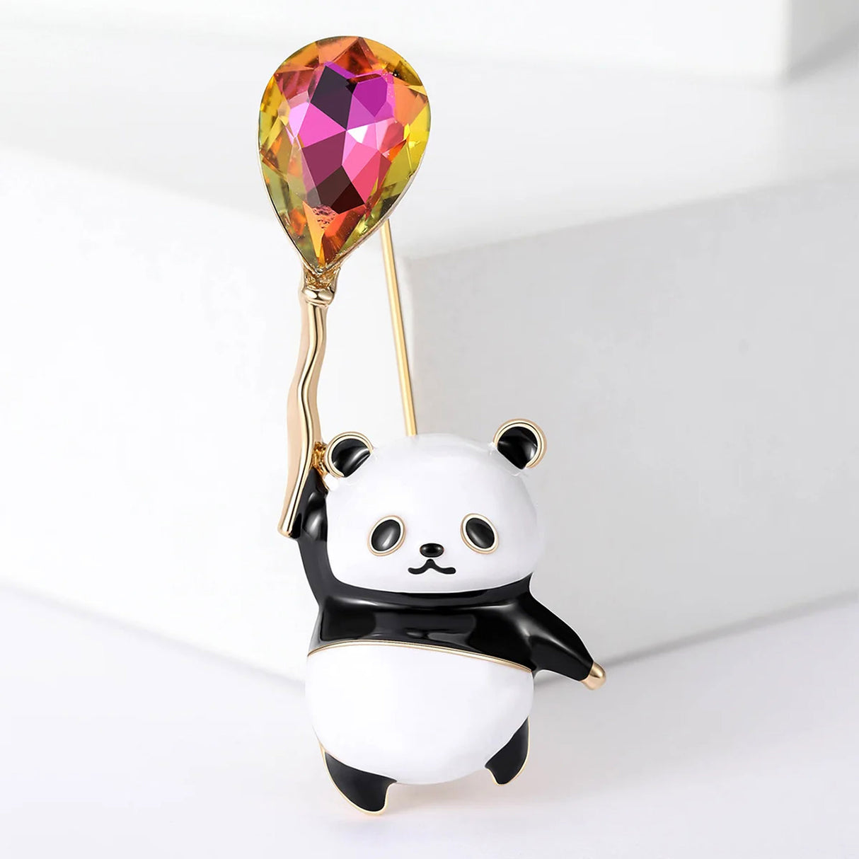 Panda brooch with black and white enamel, holding a multicolor orange-pink faceted balloon stone, front studio view.