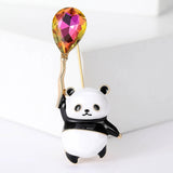 Panda brooch with black and white enamel, holding a multicolor orange-pink faceted balloon stone, front studio view.