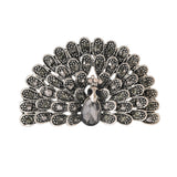 Peacock brooch with black faceted stones and silver-tone base, teardrop center stone, cutout on white.