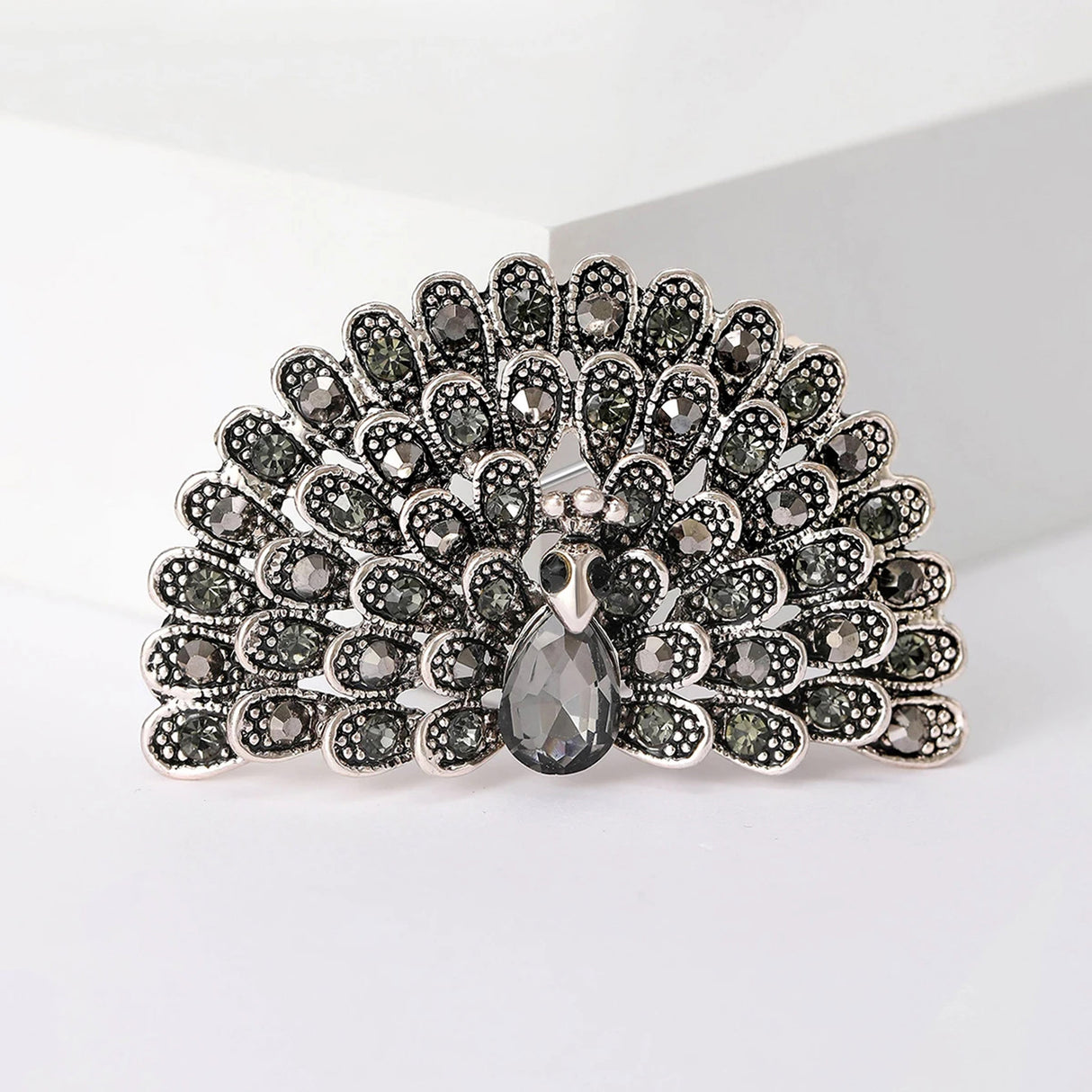 Peacock brooch set in silver-tone metal with black stones in a fan shape and a teardrop center stone, cutout on white.