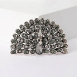 Peacock brooch set in silver-tone metal with black stones in a fan shape and a teardrop center stone, cutout on white.