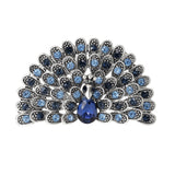 Peacock brooch with light and dark blue faceted stones, silver-tone metal, and blue teardrop center stone, cutout on white.