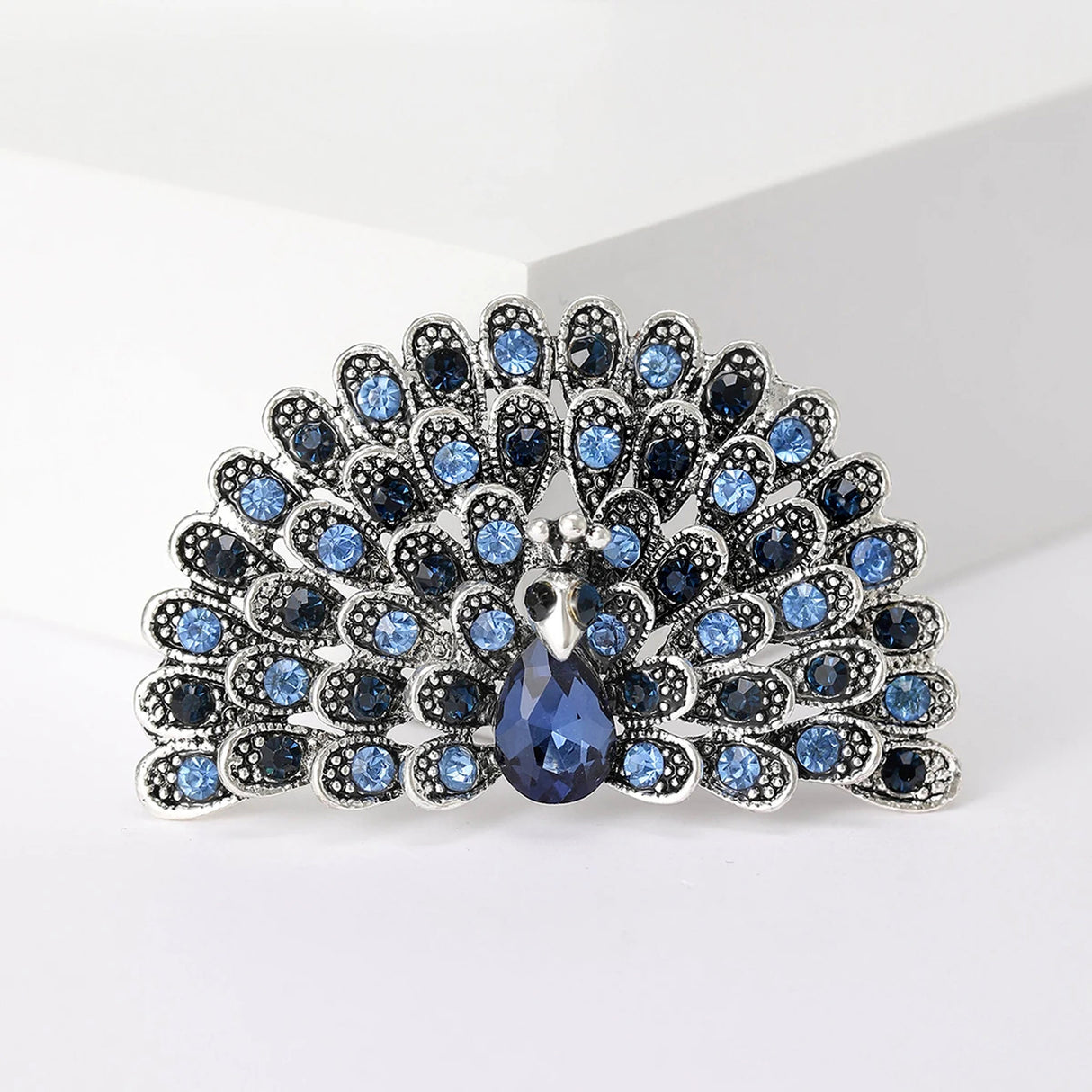Peacock brooch in silver-tone with alternating light and dark blue stones and faceted teardrop centerpiece, cutout view.