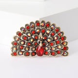 Peacock brooch with gold-tone metal, red and iridescent stones, and faceted red teardrop center, cutout studio view.