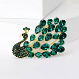 Peacock brooch with gold-tone metal, green teardrop faceted stones, and small round stones, upright view on white.