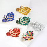 Set of six peacock brooches in multicolor, red, blue, green, yellow, and white variants, flat lay on white blocks.