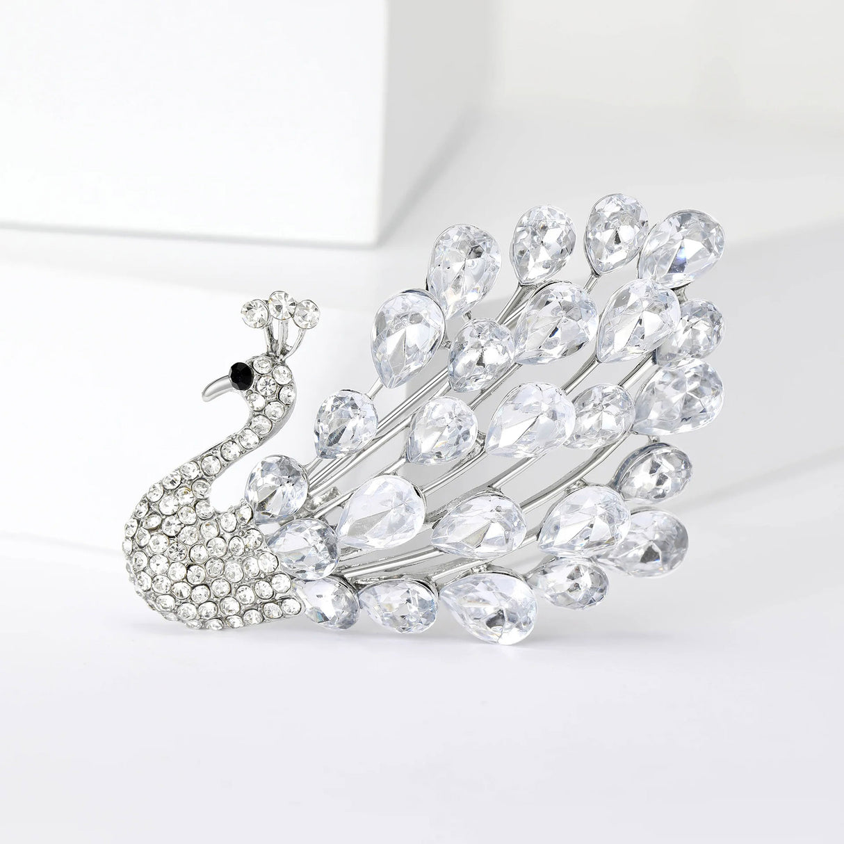 Peacock brooch with clear teardrop faceted stones and silver-tone base, upright pose on white background.