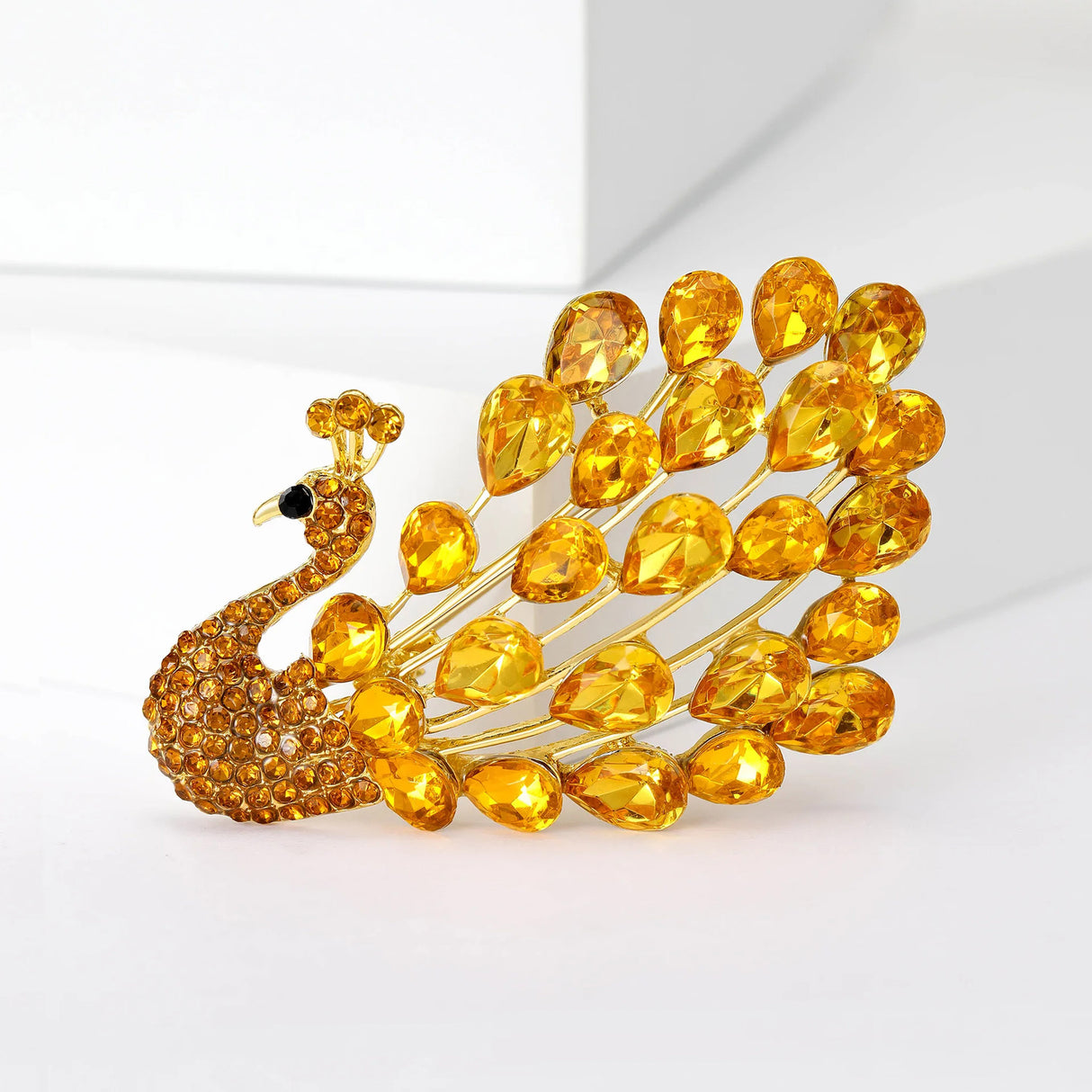 Peacock brooch with yellow teardrop faceted stones and small round stones on gold-tone base, upright on white.