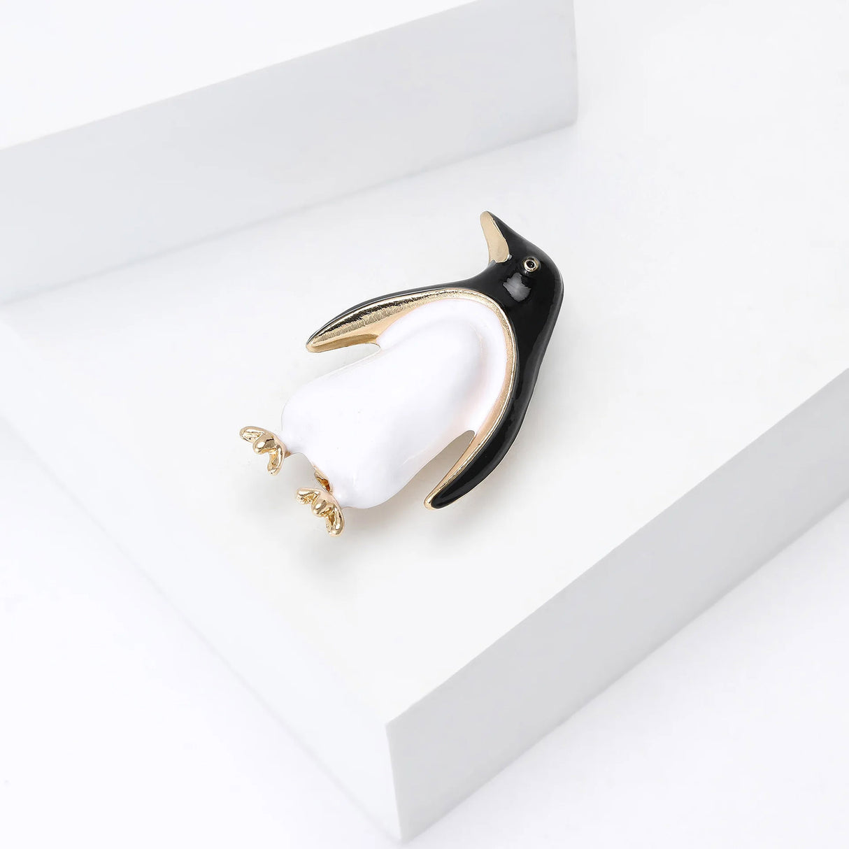 Penguin brooch with black and white enamel finish, gold-tone trim, and gold-tone feet, angled view on white platform.