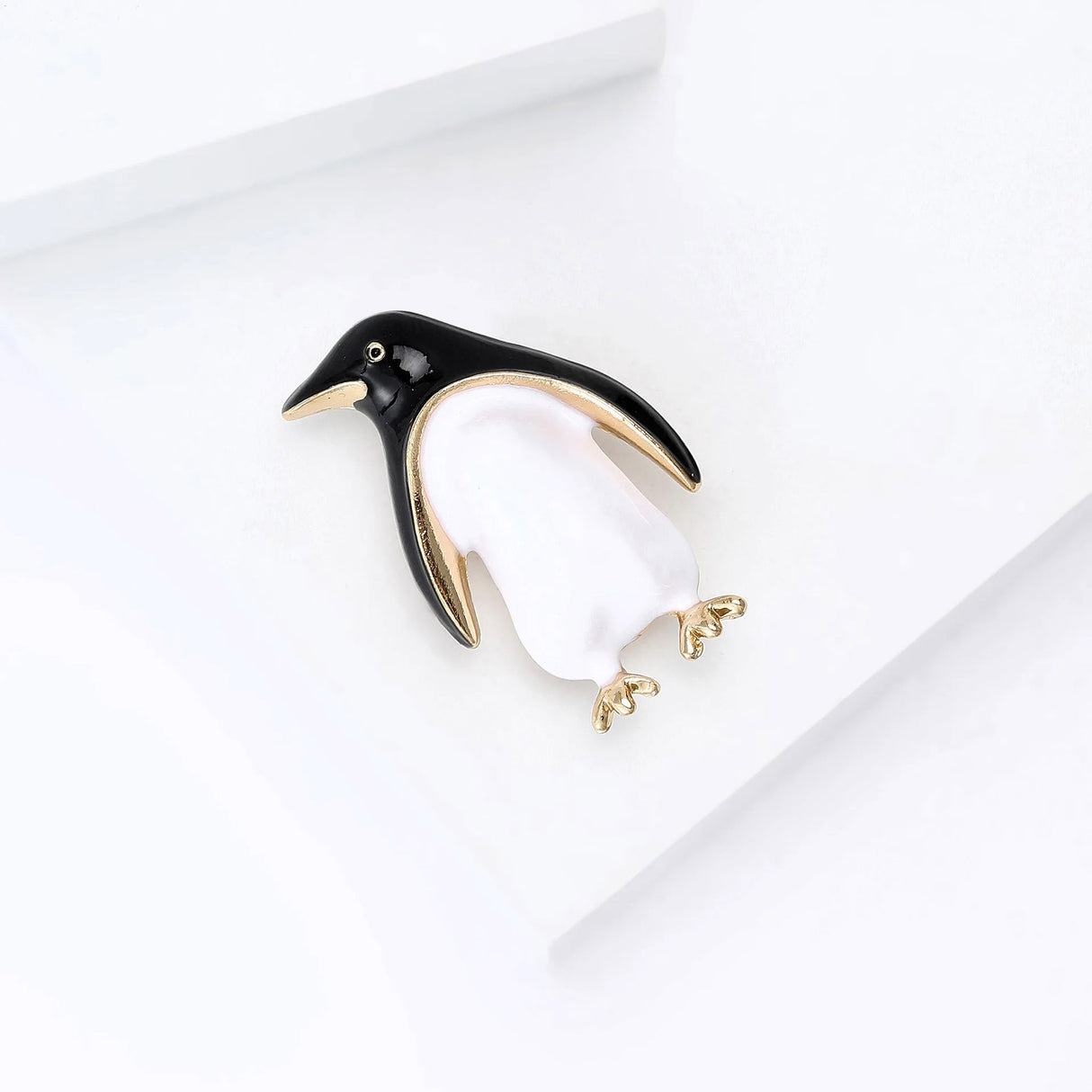 Penguin brooch featuring black and white enamel body with gold-tone details and feet, angled top-down view on white.