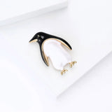 Penguin brooch featuring black and white enamel body with gold-tone details and feet, angled top-down view on white.