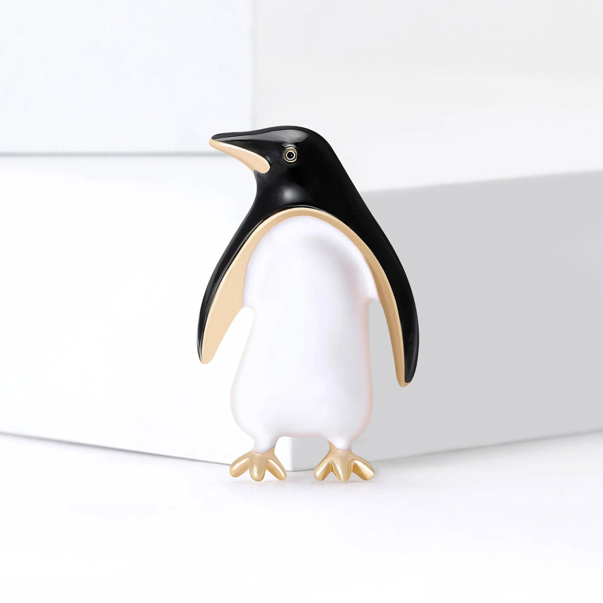 Penguin brooch with black enamel head and wings, white body, and gold-tone feet, standing pose on white surface.