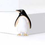 Penguin brooch with black enamel head and wings, white body, and gold-tone feet, standing pose on white surface.