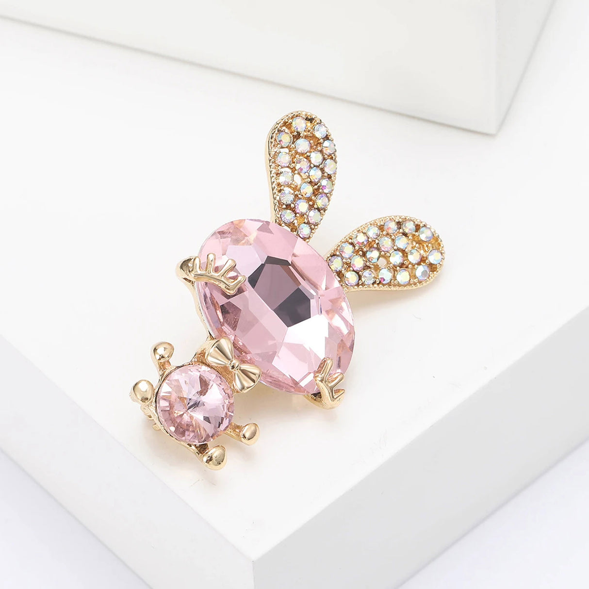 Bunny brooch featuring pink faceted stones, gold-tone accents, and crystal-studded ears, angled view on white surface.